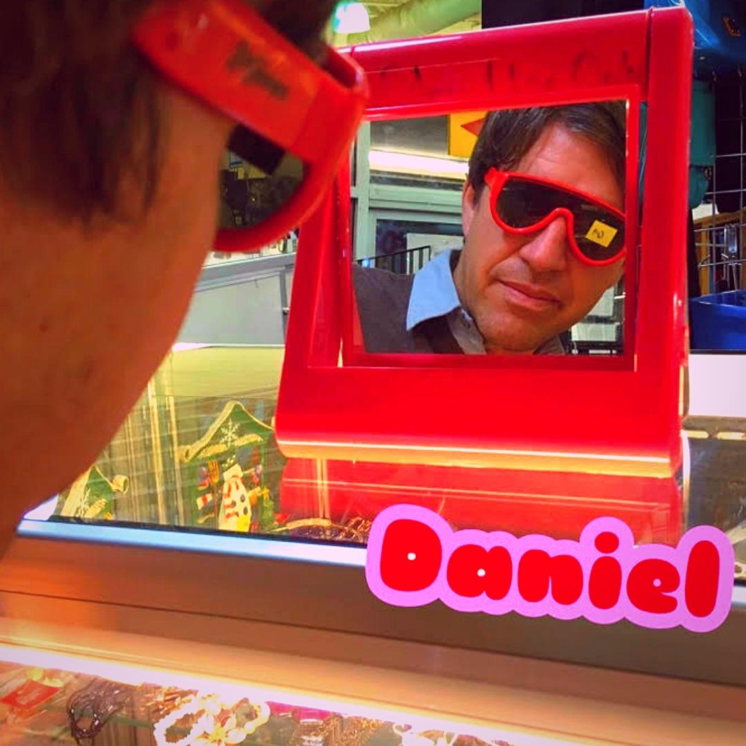 Daniel tries on a pair of red sunglasses in a colorful store.