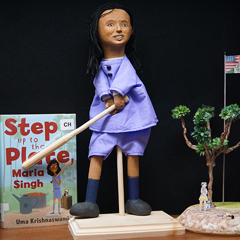 puppet of a girl swinging a bat next to a book