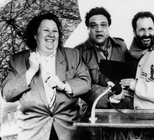 Jackie Goldberg, at left, with others at a podium on a rainy day