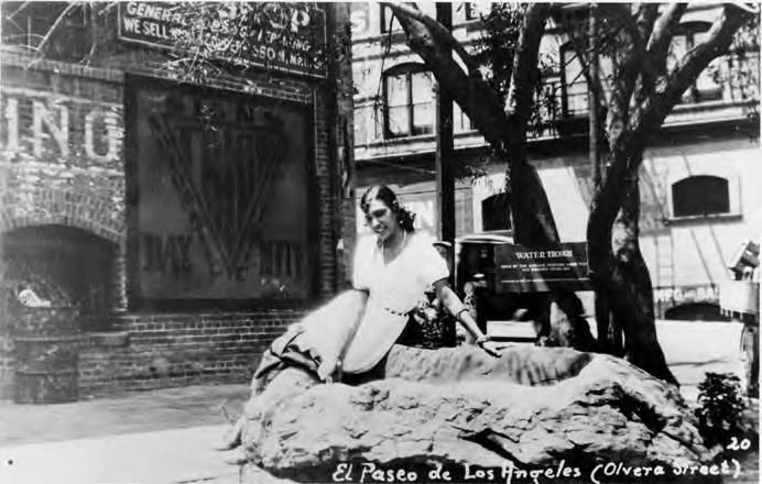 Postcard of girl sitting on water trough at north end of Olvera Street, Italian Hall at left.