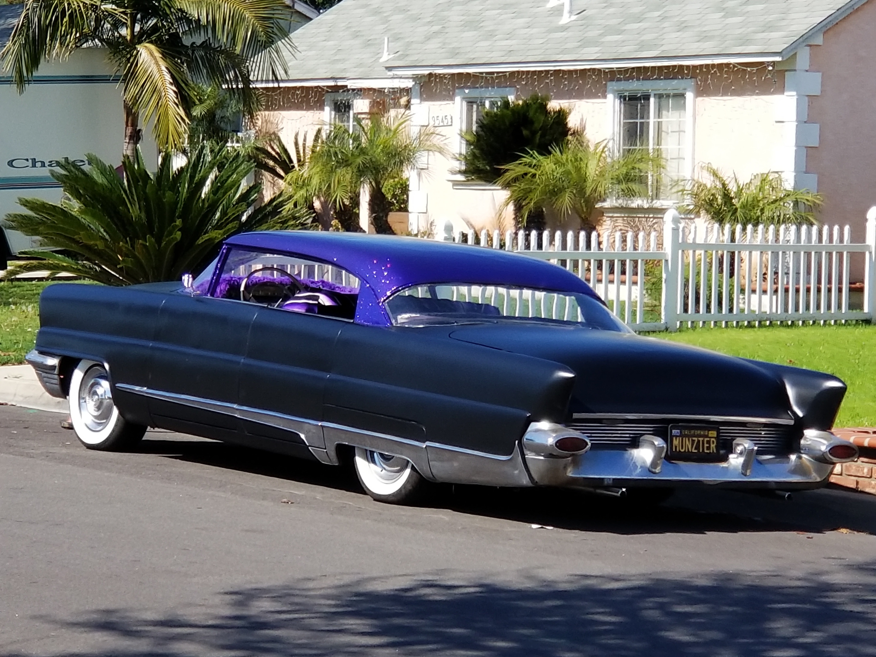purple lowrider car by a white picket fence
