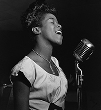 a side profile black and white photo of a young singing and smiling Sarah Vaughan