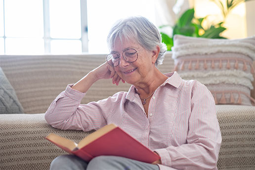Smiling senior woman relaxing sitting on the floor reading a book.