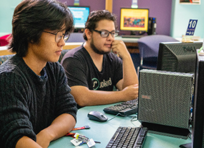 Two students work on computers in the library.