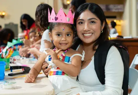 child with paper crown sits on parent's lap