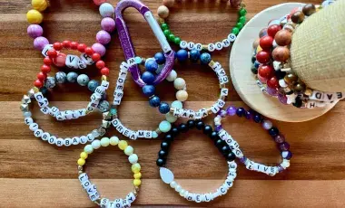 Multicolored, beaded friendship bracelets are arrayed on a wooden table.