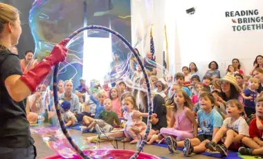 Adult holding a hula hoop, making bubbles, in front of a crowd of children
