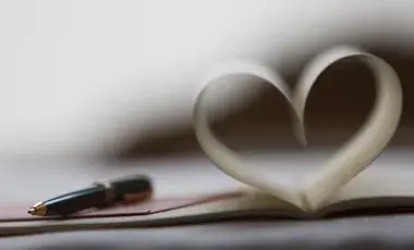 A black pen rests on an open book with pages folded to resemble a heart shape
