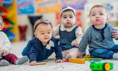 Four babies sitting up on the floor with toys in front of them
