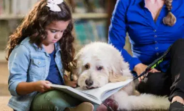 a child reading to a dog with an adult in the background
