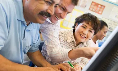 a man helps another man on a computer while a woman looks on