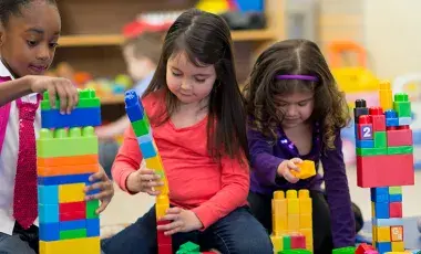 Three girls build with Lego building blocks.