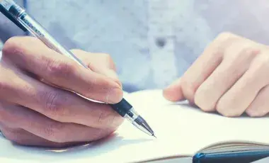Two hands, one writing in a notebook.