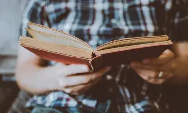 Man holding a book while wearing a plaid shirt