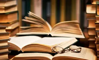 Stacks of closed and open books with a pair of glasses resting on top.