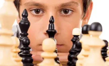 Young boy looking at chess pieces.