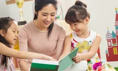 Young female teacher, volunteer reads to a group of smiling young kids.