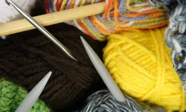 A collection of multicolored skeins of wool and knitting needles.