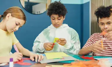 Three children cutting pieces of colorful construction paper. 