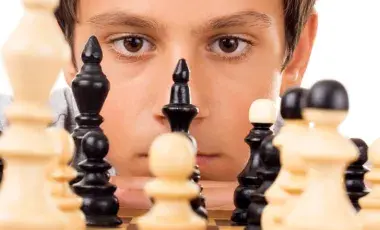 a young male peers across a black and white chess board