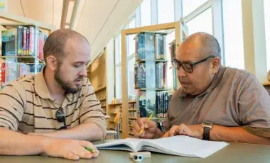 Two men sitting at a table looking at a book.