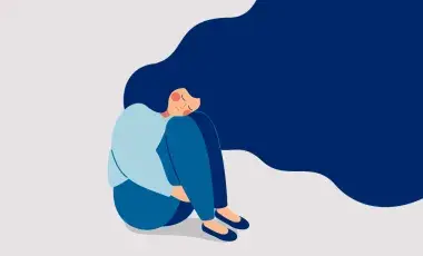 Person with flowing blue hair wearing a light blue top and blue pants is seated tucking her body into a ball as if she is stressed, depressed, or overwhelmed.