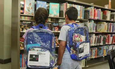 Two children wear clear backpacks filled with play kits.