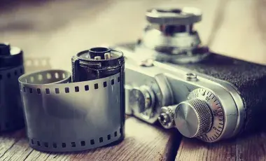 Close up photo of a camera and two rolls of 35mm film on a wooden surface.