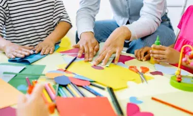 Art supplies strewn across a table with people creating. 