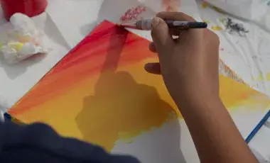 a person's hand is painting a sunset on canvas