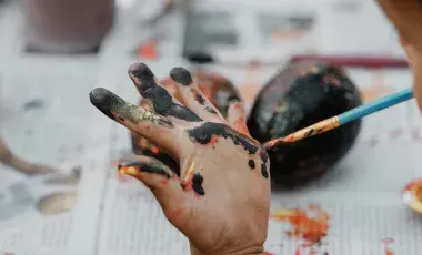 A child painting their own hand with a paintbrush.