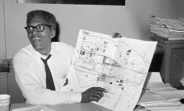 Bayard Rustin holding up a city map and pointing at it.