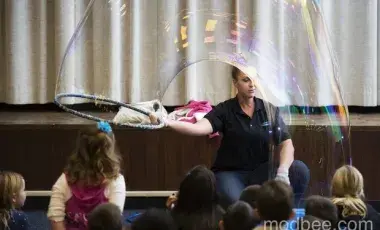 A Bubblologist makes a huge bubble in front of children.