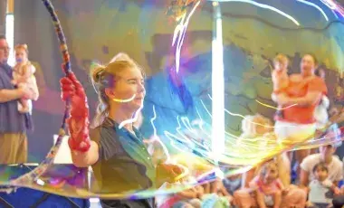 Instructor making a big bubble with a big hoop while families watch.