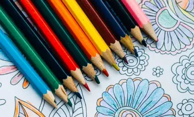 Photo is of different colored pencils on top of a colored in page with designs.