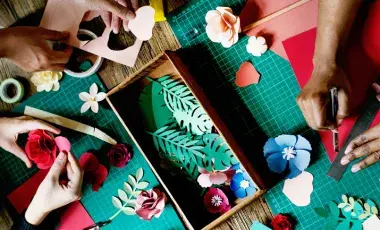Three pairs of hands use crafting tools to make paper flowers.