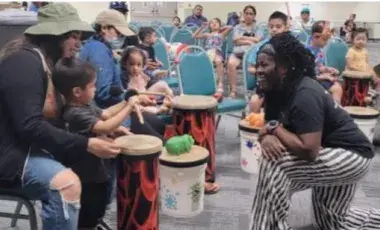 Woman kneeling in front of a mother and child playing a drum