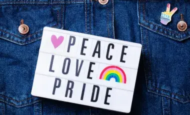 A jean jacket with a peace pride button on its pocket and a sign that says "peace, love, pride."