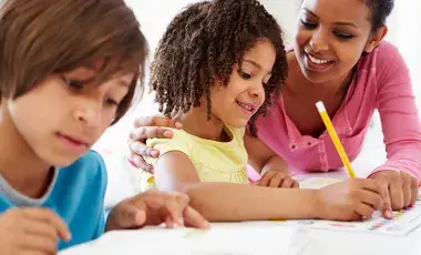 Adult assisting a child with written homework while another student works nearby