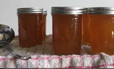 a spoon and four jars of jam atop a plaid tablecloth 
