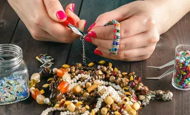 Hands with painted red nails using tools and beads to make a jewelry piece.