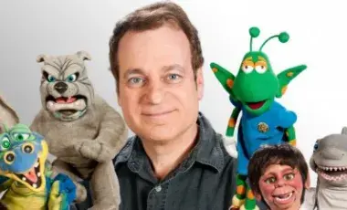 A smiling man is surrounded by colorful puppets