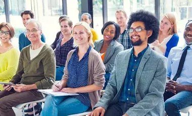 A group of adult learners smiling and practicing English pronunciation and everyday idioms together in a library classroom.