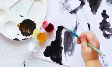 a young child's hand is using a brush to paint with black paint