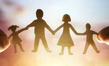 Silhouette of a paperdoll family being held by two hands against a bright background.