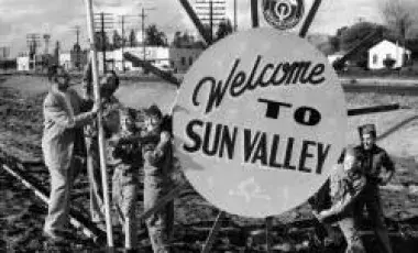 black and white photo of people around sign that reads welcome to sun valley
