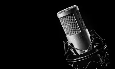 A closeup of a podcasting microphone against a black background.