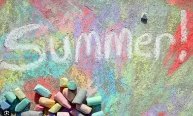 Colorful sidewalk chalk art with the word “Summer!” written on pavement beside scattered chalk pieces.