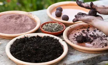Hands rolling clay and compost seed bombs beside trays of soil and seeds.