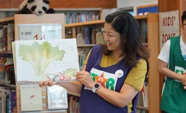 Woman holding up a book smiling and reading. 